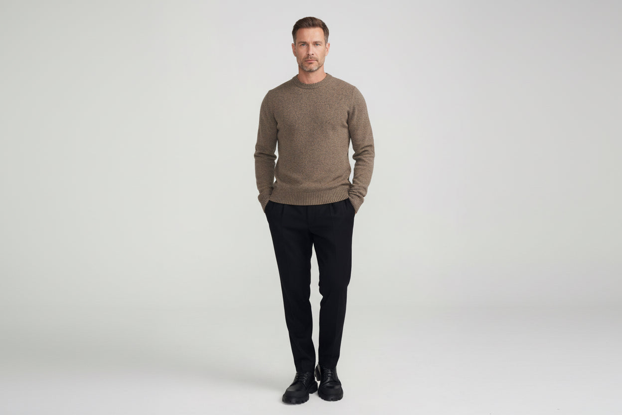 A man wearing a brown wool blend sweater with ribbed cuffs and neckline, paired with black trousers and black shoes.