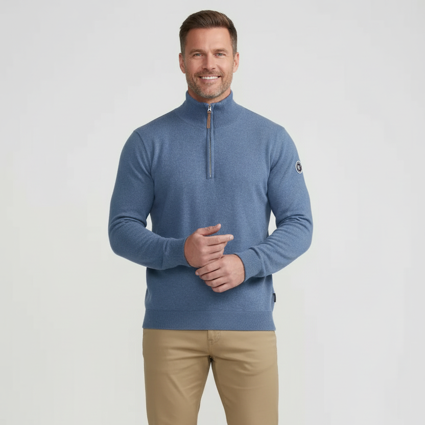 A male model wearing a fade blue, quarter zip, long-sleeved sweater with ribbed high collar and endings.